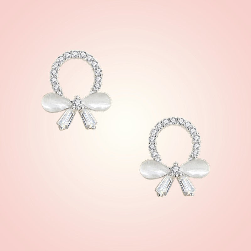 Pair of bow-shaped earrings with crystals on a pink background