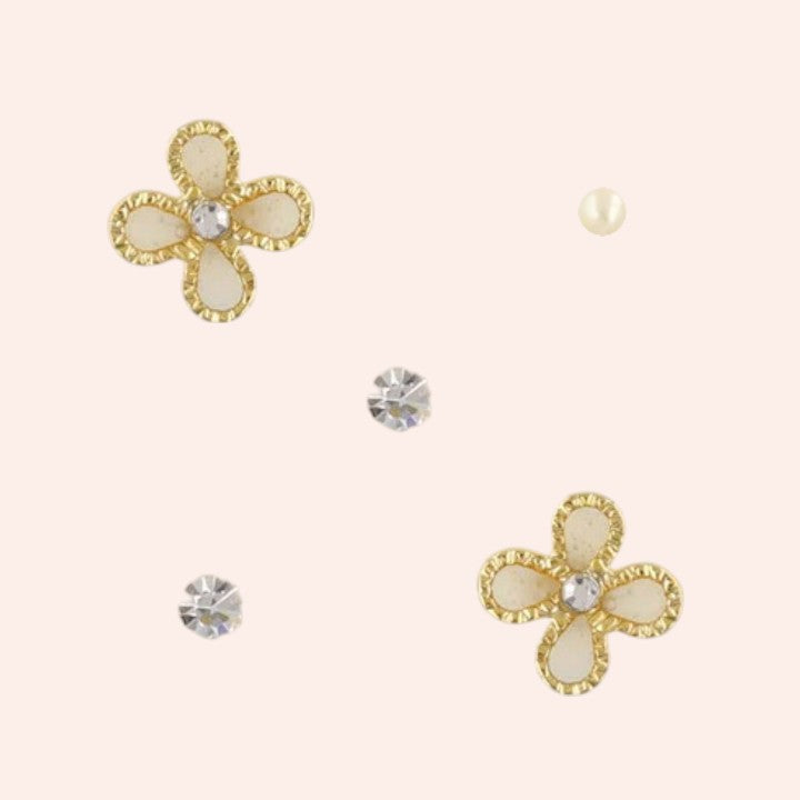 Flower-shaped earrings with gold and pearl-like details on a beige background