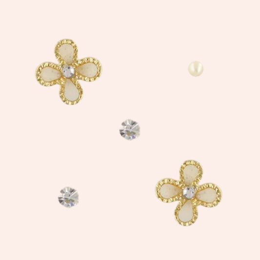 Flower-shaped earrings with gold and pearl-like details on a beige background