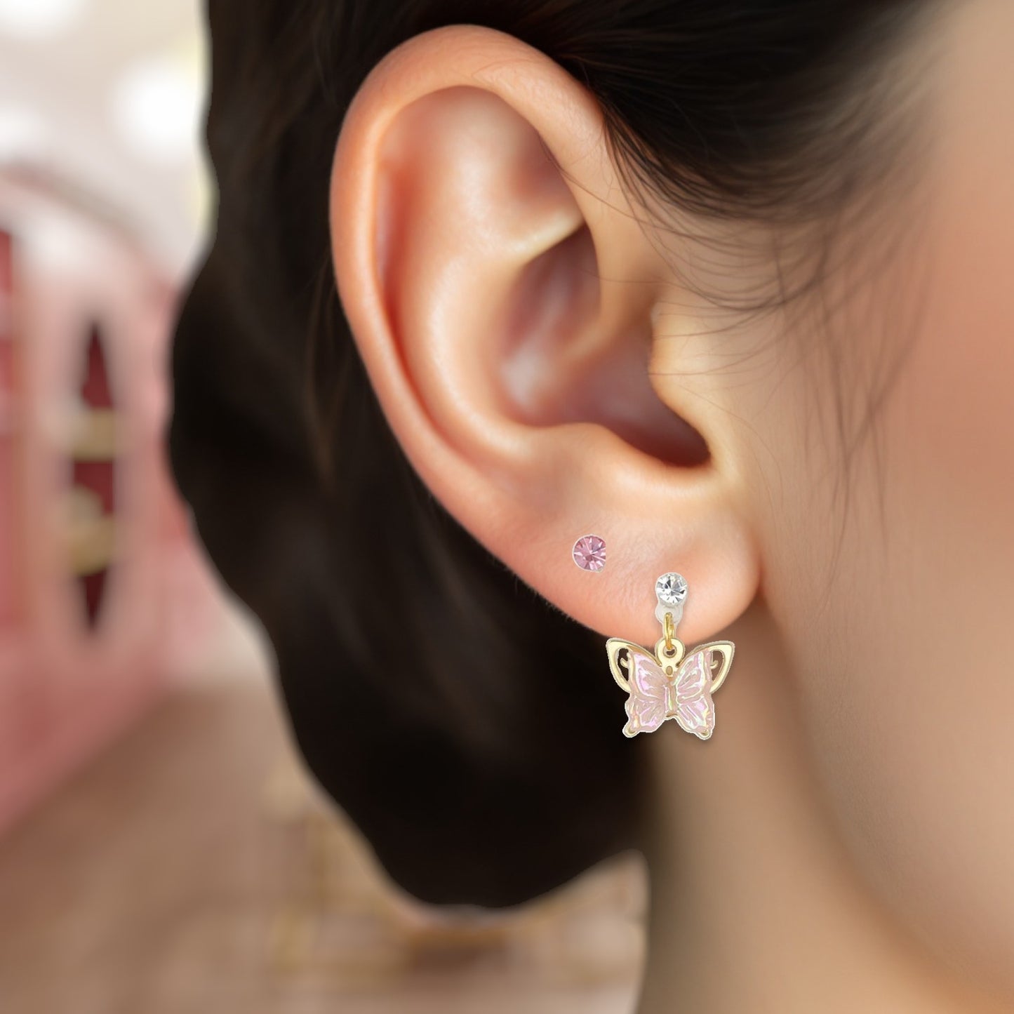 Close-up of an ear wearing a butterfly-shaped earring with a pink gemstone.