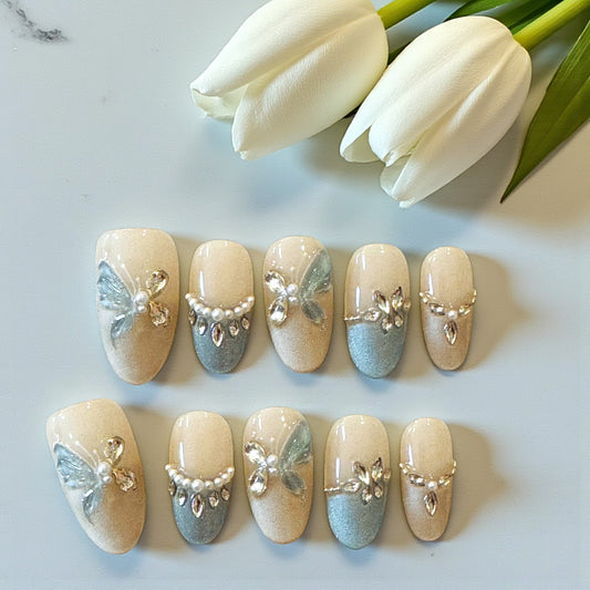 Decorative nail art with butterflies and pearls on a white surface with tulips in the background