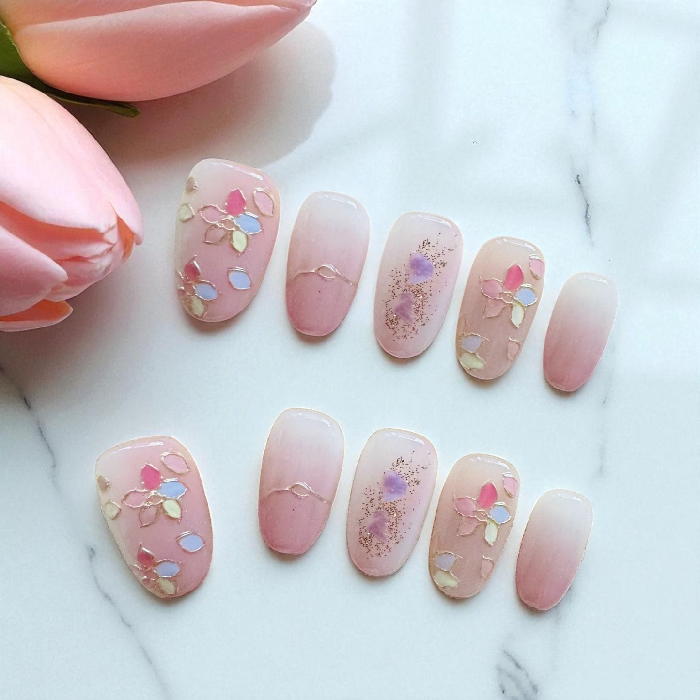 Pink nail art with floral designs on a marble surface with pink tulips.