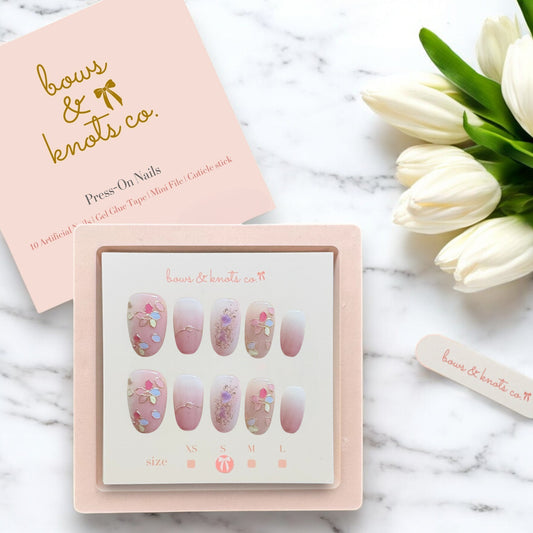 Set of press-on nails with a 'bows & knots co.' box on a marble surface with tulips.