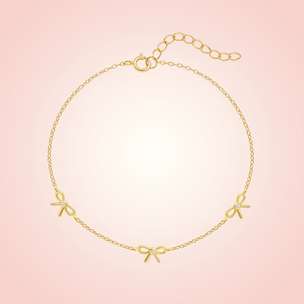 Gold bracelet with bow-shaped charms on a pink background
