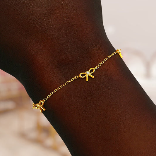 Gold bracelet with bow-shaped charms on a wrist against a blurred background