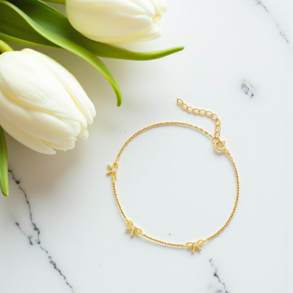 Gold bracelet with small charms on a marble surface with white tulips.