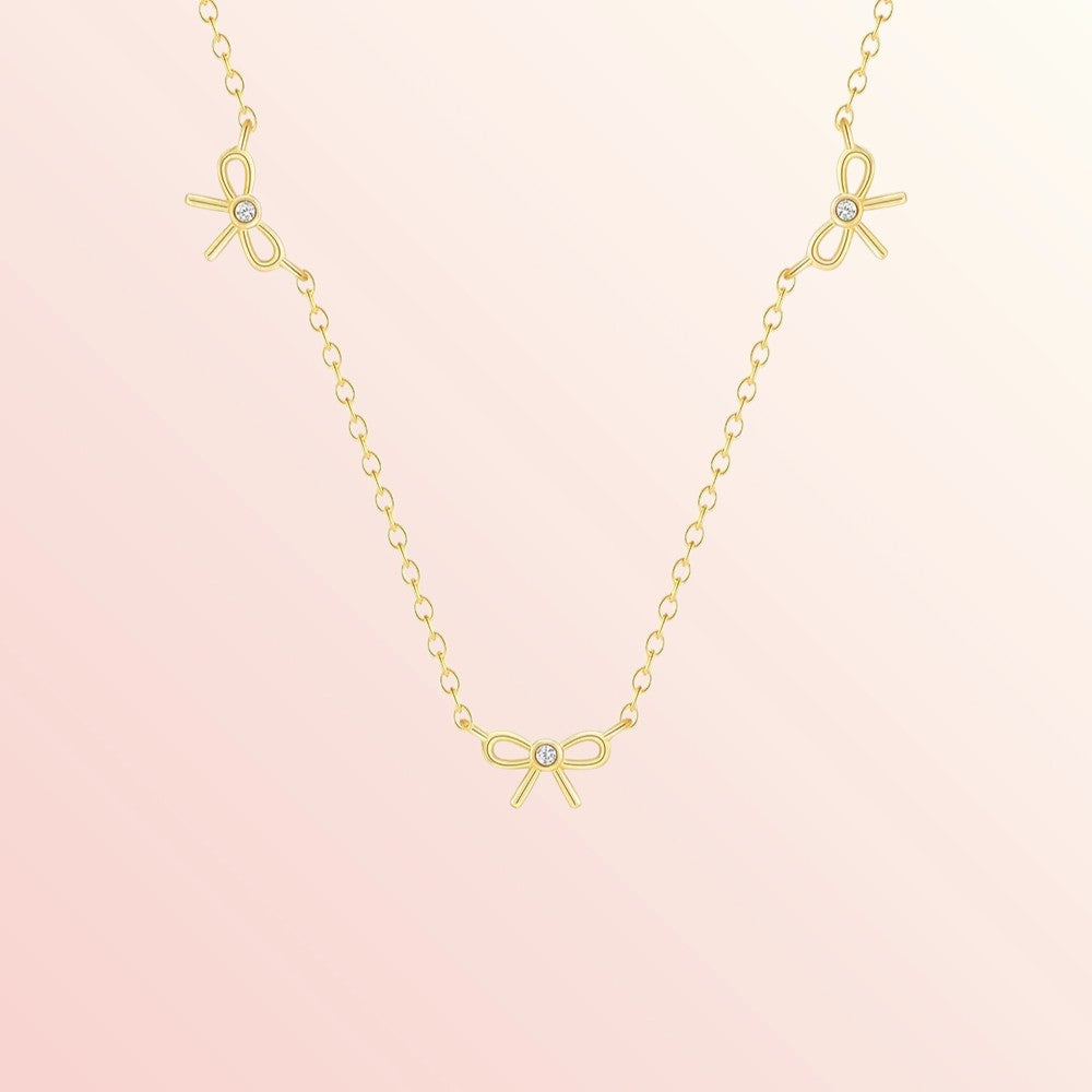 Gold necklace with bow-shaped pendants on a pink background