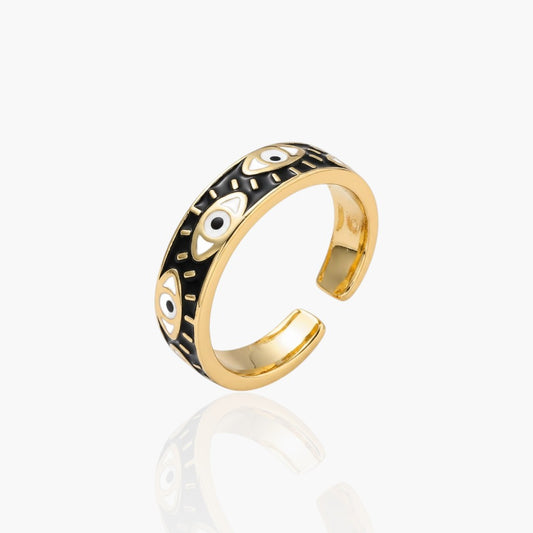 Gold-plated open ring band featuring a black enamel inlay with white and black evil eye motifs, shown on a light gray background with a soft reflection.