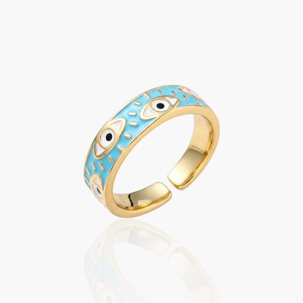 A gold-plated open band ring featuring a light blue enamel inlay decorated with white and black evil eye motifs, shown on a clean white background with a soft reflection.