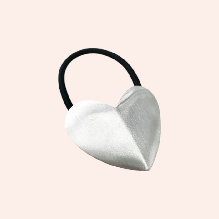 Heart-shaped hair tie with a metallic finish on a light pink background