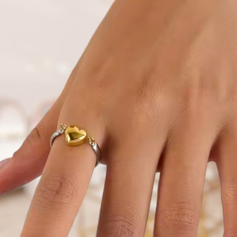 Hand wearing a gold heart-shaped ring on a neutral background