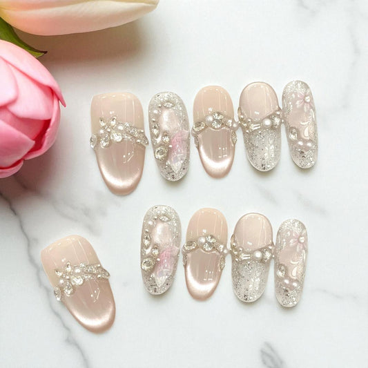 Decorative false nails with rhinestones on a marble surface with pink flowers.