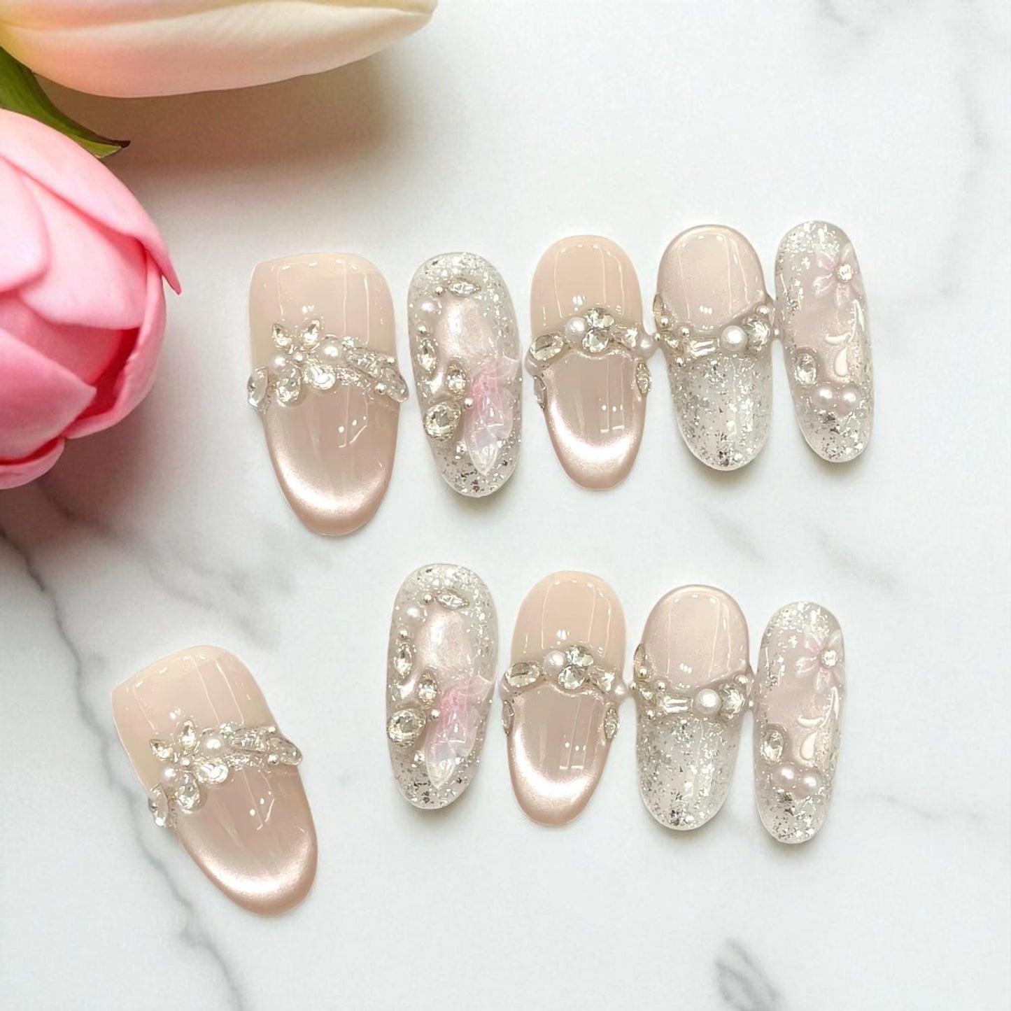 Decorative false nails with rhinestones on a marble surface with pink flowers.