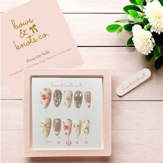 Press-on nails set with packaging and floral decorations on a wooden surface
