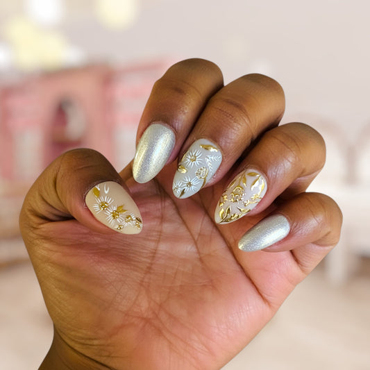 Hand with decorative nails featuring gold and silver designs on a blurred background