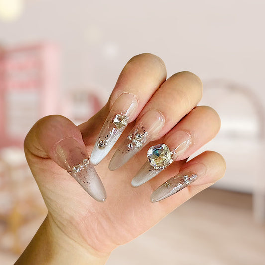 Hand with decorative nails featuring crystals and a gemstone on a blurred background