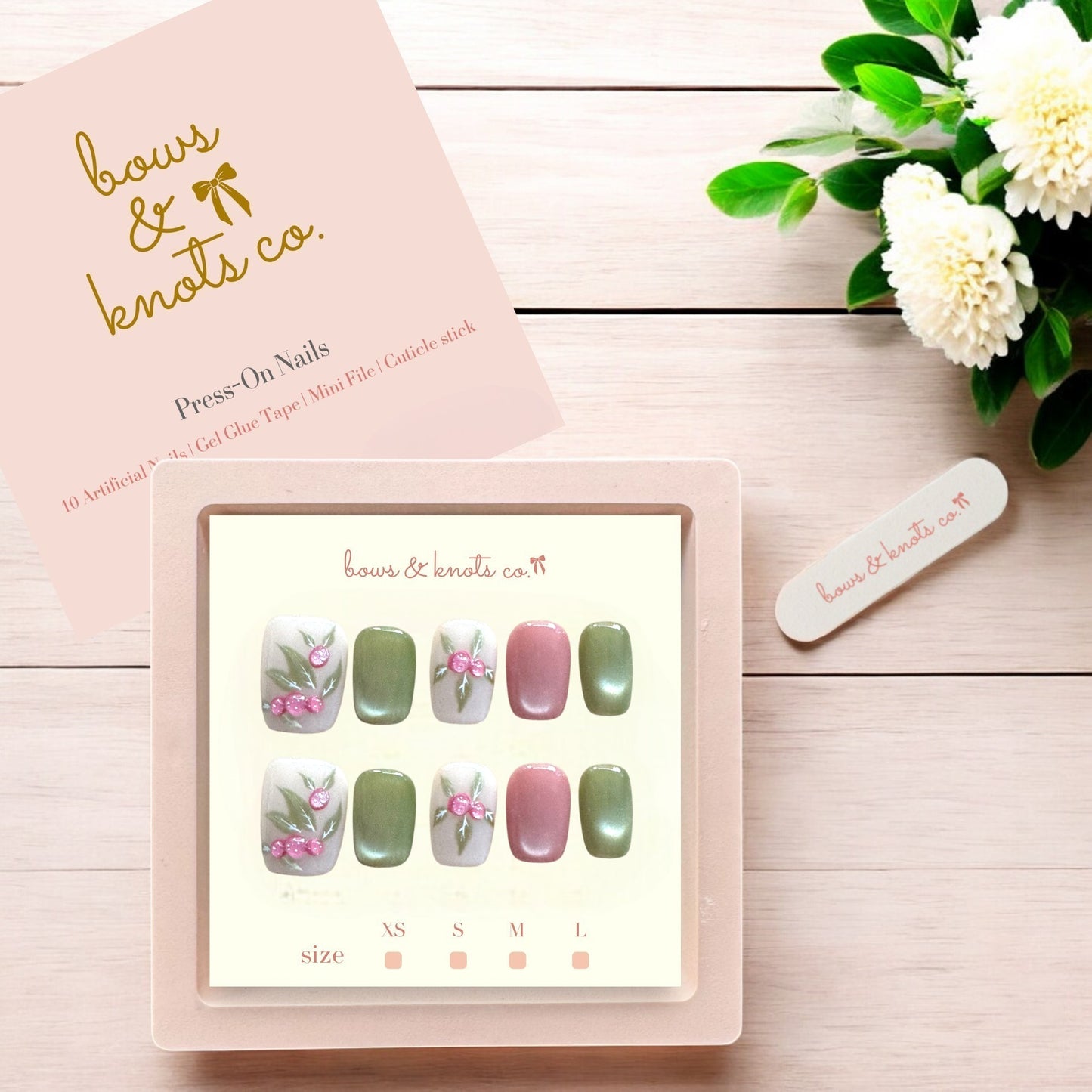 Set of press-on nails with a 'bows & knots co.' box on a wooden surface with flowers.
