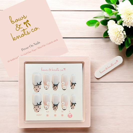 Set of press-on nails with decorative designs in a pink box on a wooden surface with flowers.