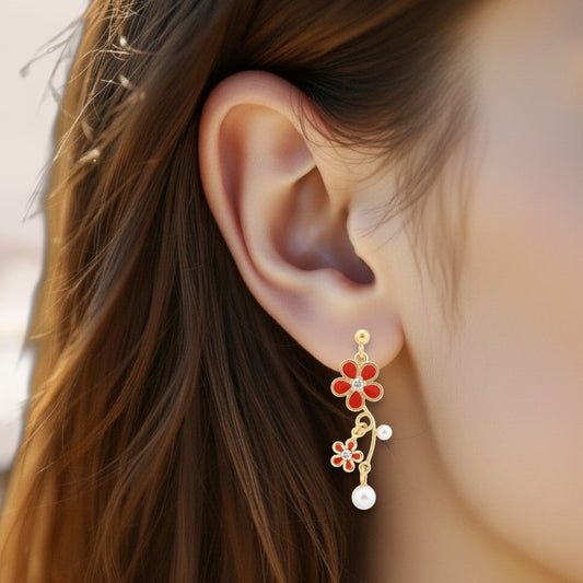 Close-up of an ear wearing a floral earring with red flowers and pearls.