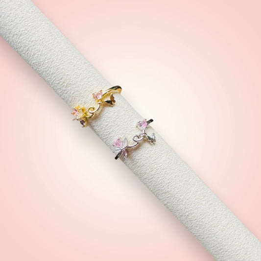 Two gold rings with pink gemstones on a textured white surface with a soft pink background