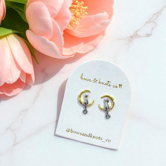 Pair of earrings on a branded card with pink flowers in the background