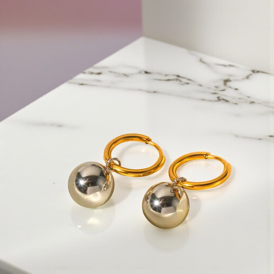 Gold hoop earrings with silver spherical charms on a marble surface