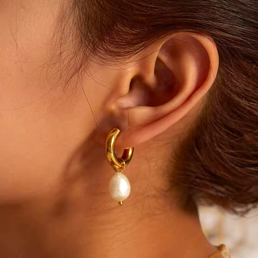 Gold hoop earring with a pearl drop worn by a person.