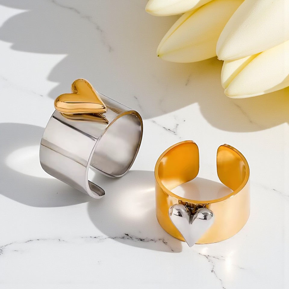 Two cuff rings, one gold and one silver, on a marble surface with a flower in the background.