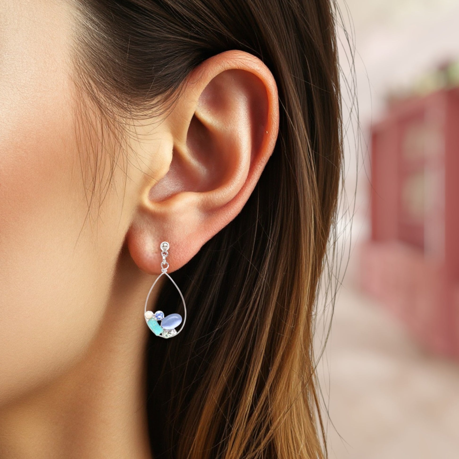 Close-up of an ear wearing a teardrop-shaped earring with colorful stones.