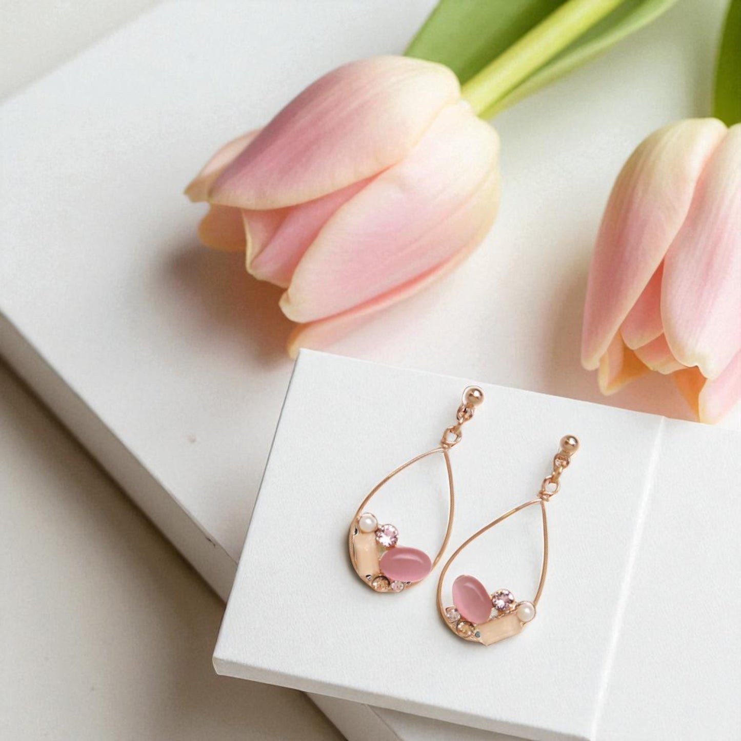 Rose gold earrings with pink stones on a white box with pink tulips in the background