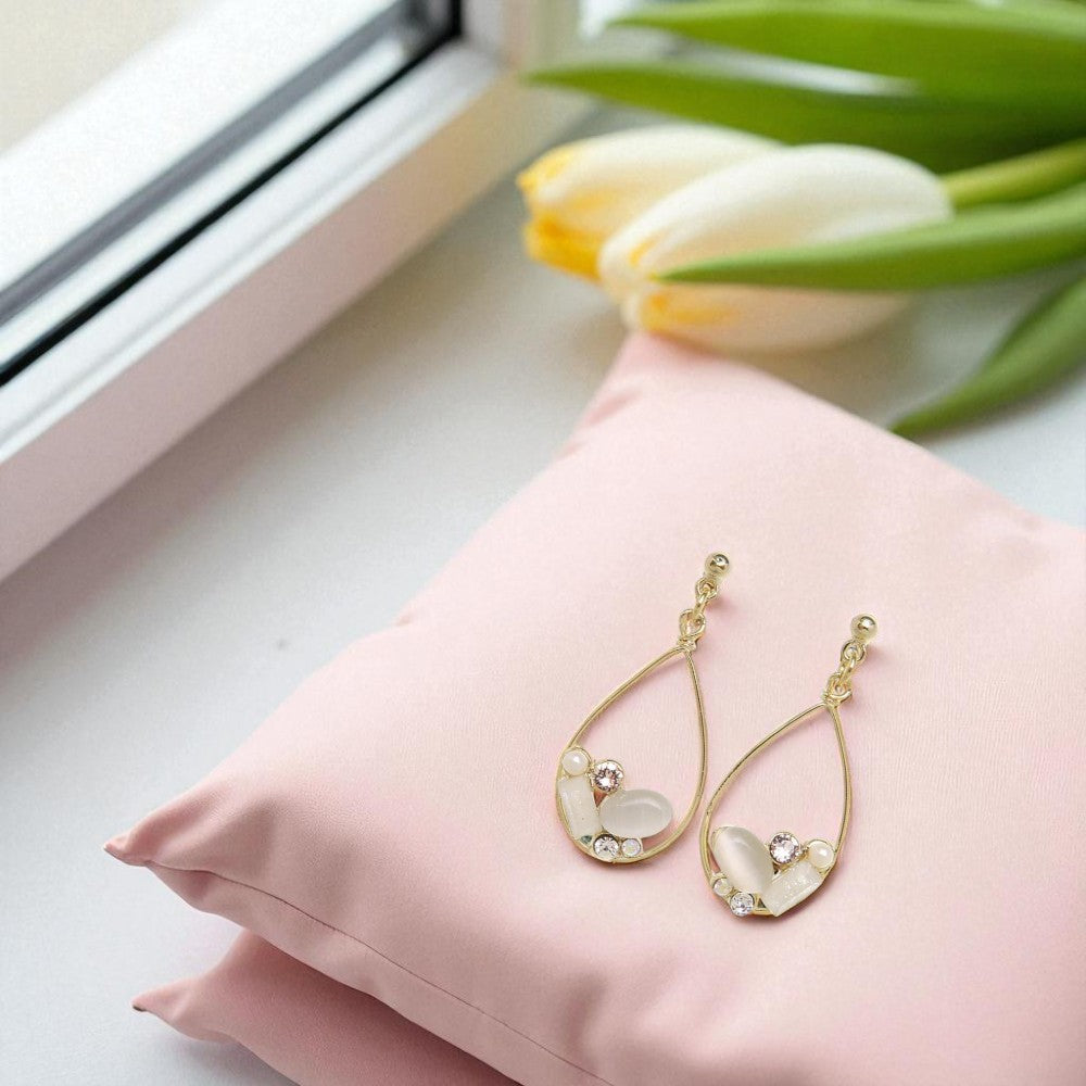 Gold earrings with leaf designs on a pink pillow next to tulips