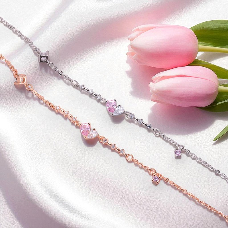 Two bracelets, one rose gold and one silver, with pink gemstones on a white surface with pink tulips.