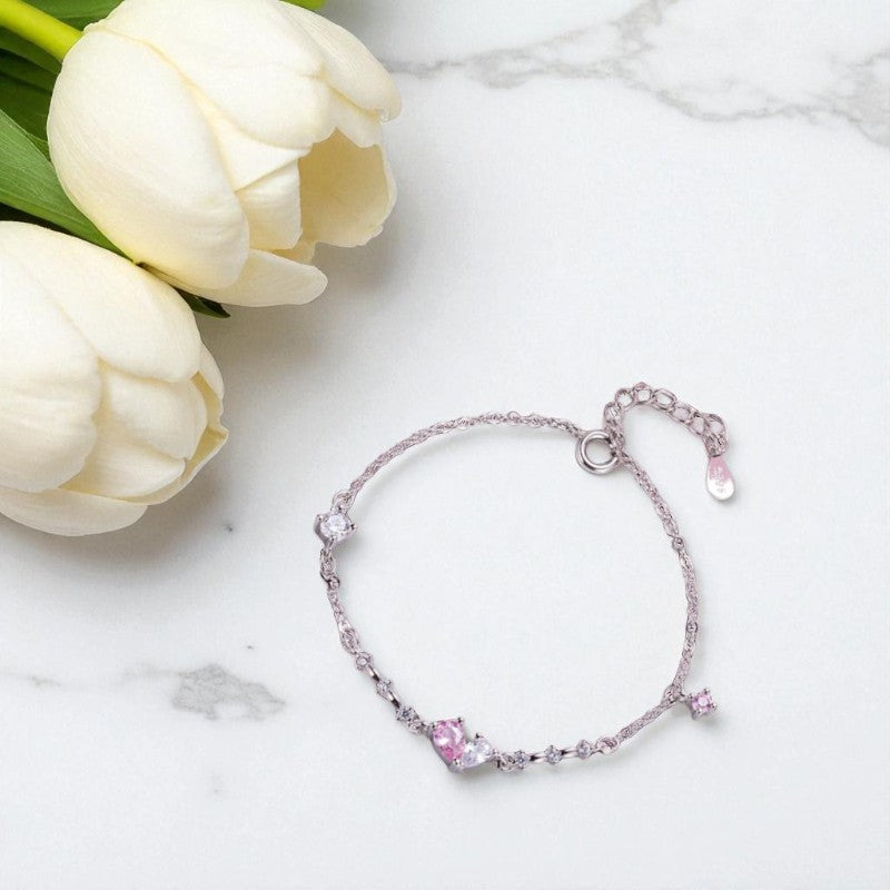 Silver bracelet with pink gemstones on a marble surface with white tulips.