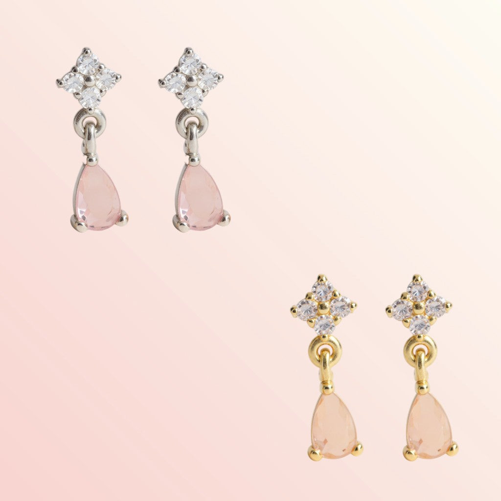Pair of earrings with pink teardrop-shaped stones and star-shaped tops on a light pink background.