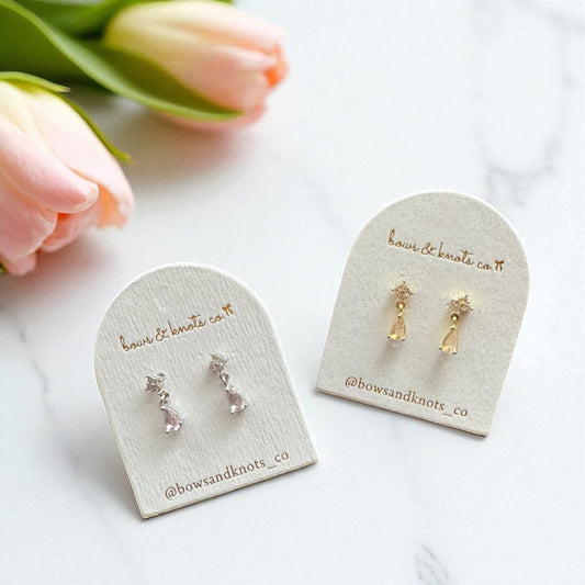 Gold earrings on branded display cards with tulips in the background