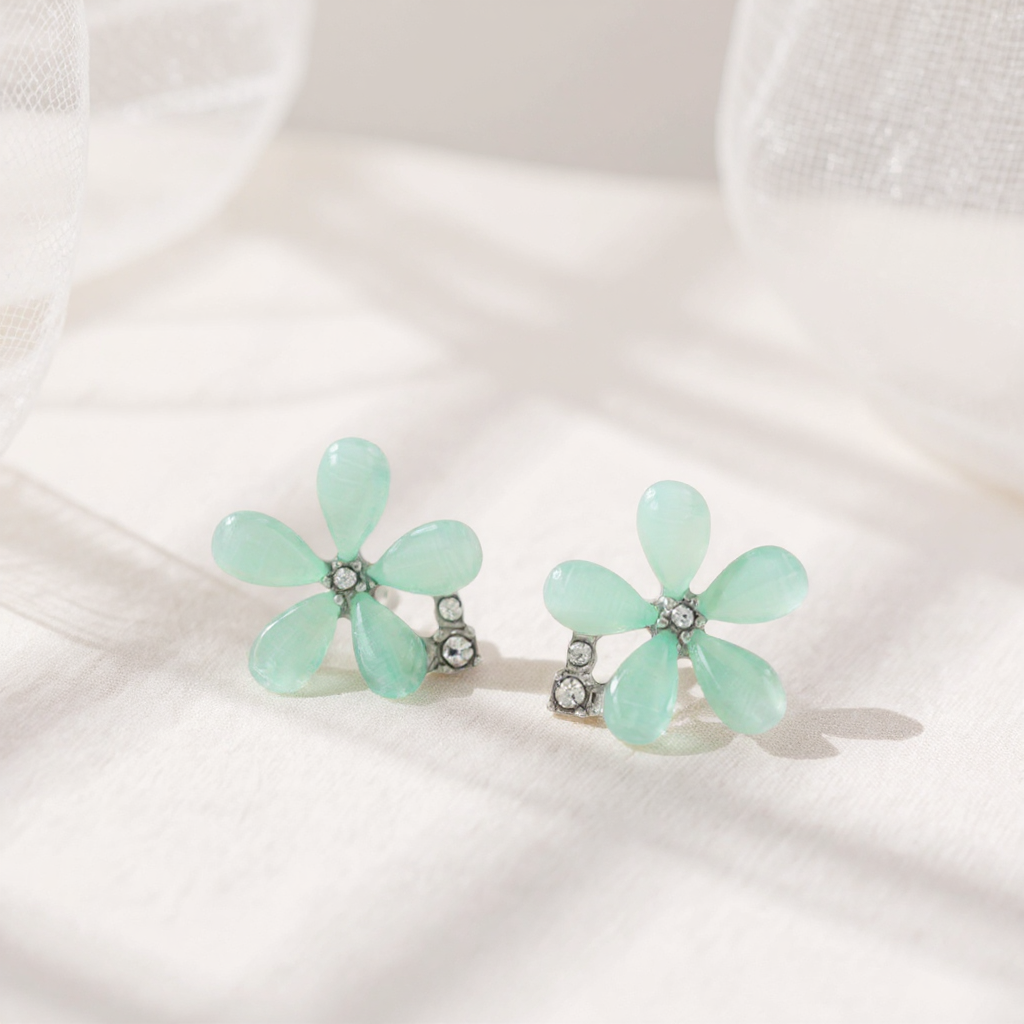 Pair of mint green flower-shaped earrings on a white fabric background
