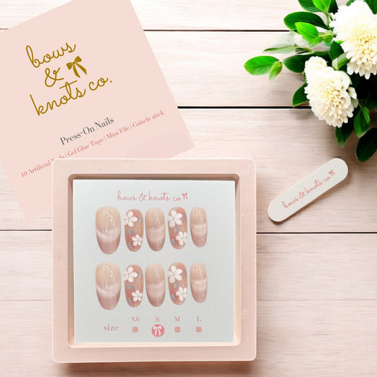 Nail art display with press-on nails and a pink box on a wooden surface with flowers.