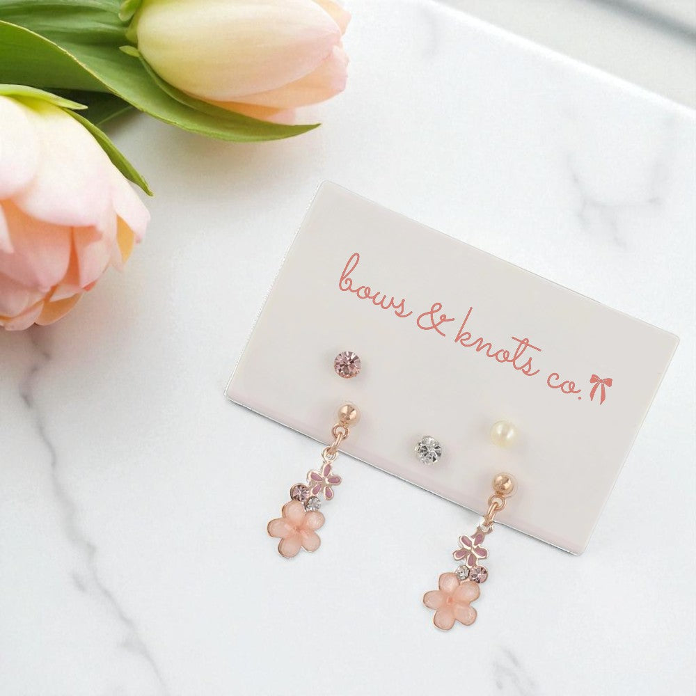 Floral earrings on a 'bows & knots co' card with flowers in the background