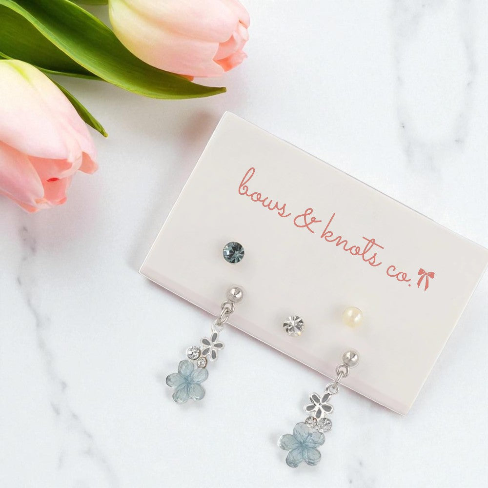 Floral earrings on a card with 'bows & knots co.' branding, surrounded by pink tulips.