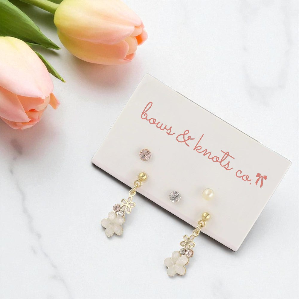 Pair of floral earrings on a 'bows & knots co.' card with pink tulips in the background.