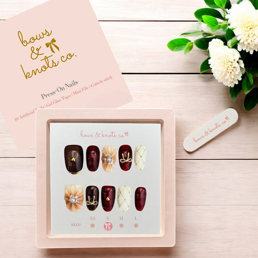 Nail art display with press-on nails and a pink box labeled 'bows & knots co.' on a wooden surface.