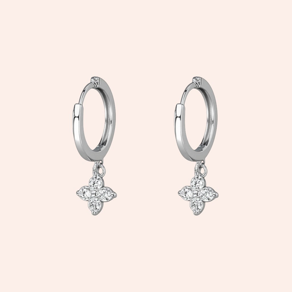 Silver hoop earrings with butterfly-shaped diamond pendants on a light pink background