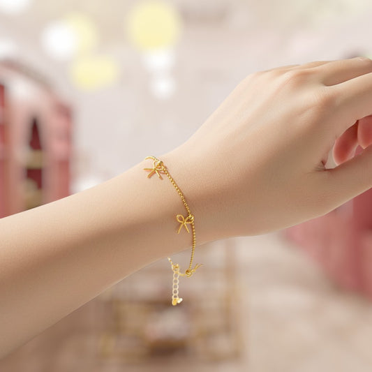 Gold bracelet with bow charm on a wrist against a blurred background