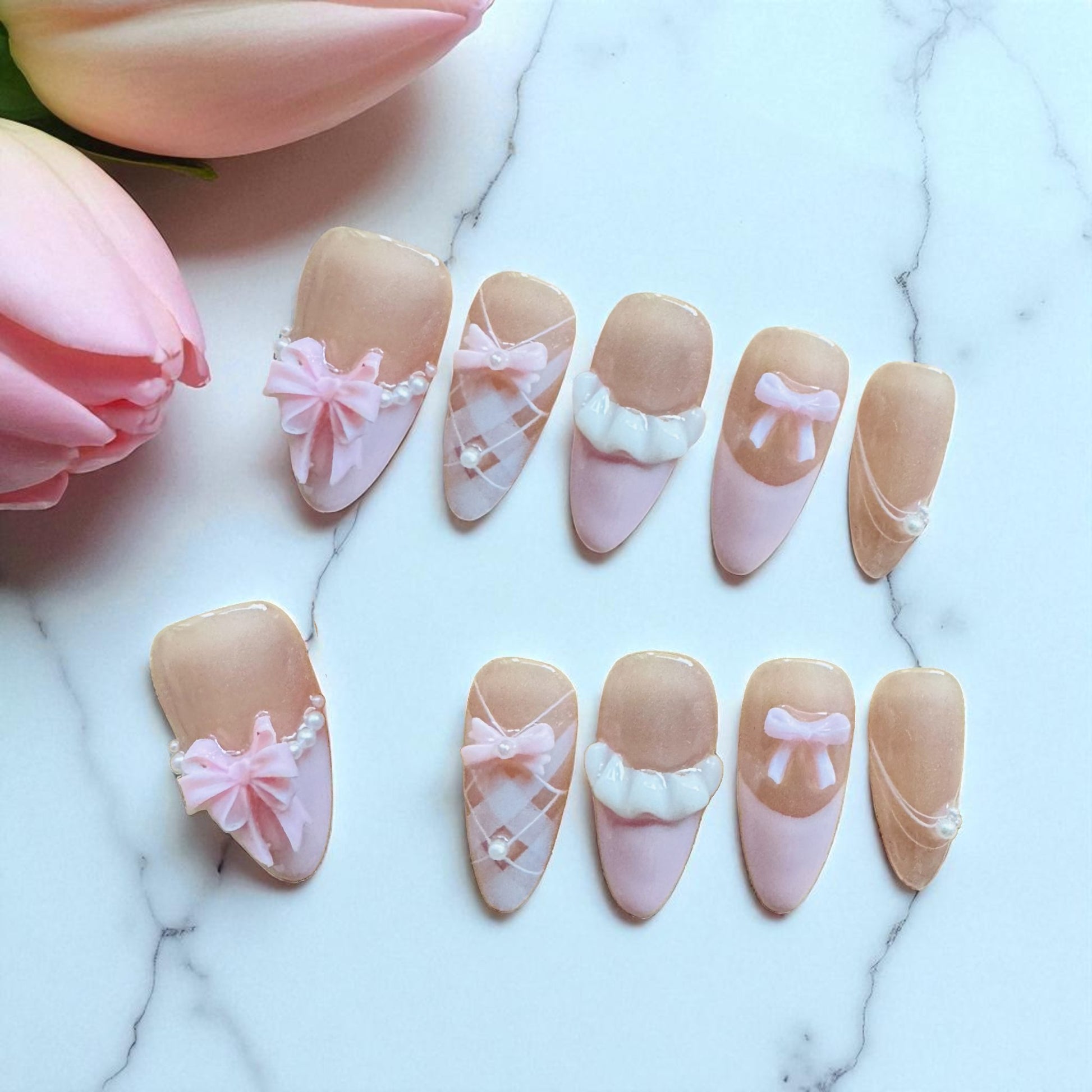 Decorative nail art with pink and beige designs on a marble surface with tulips.