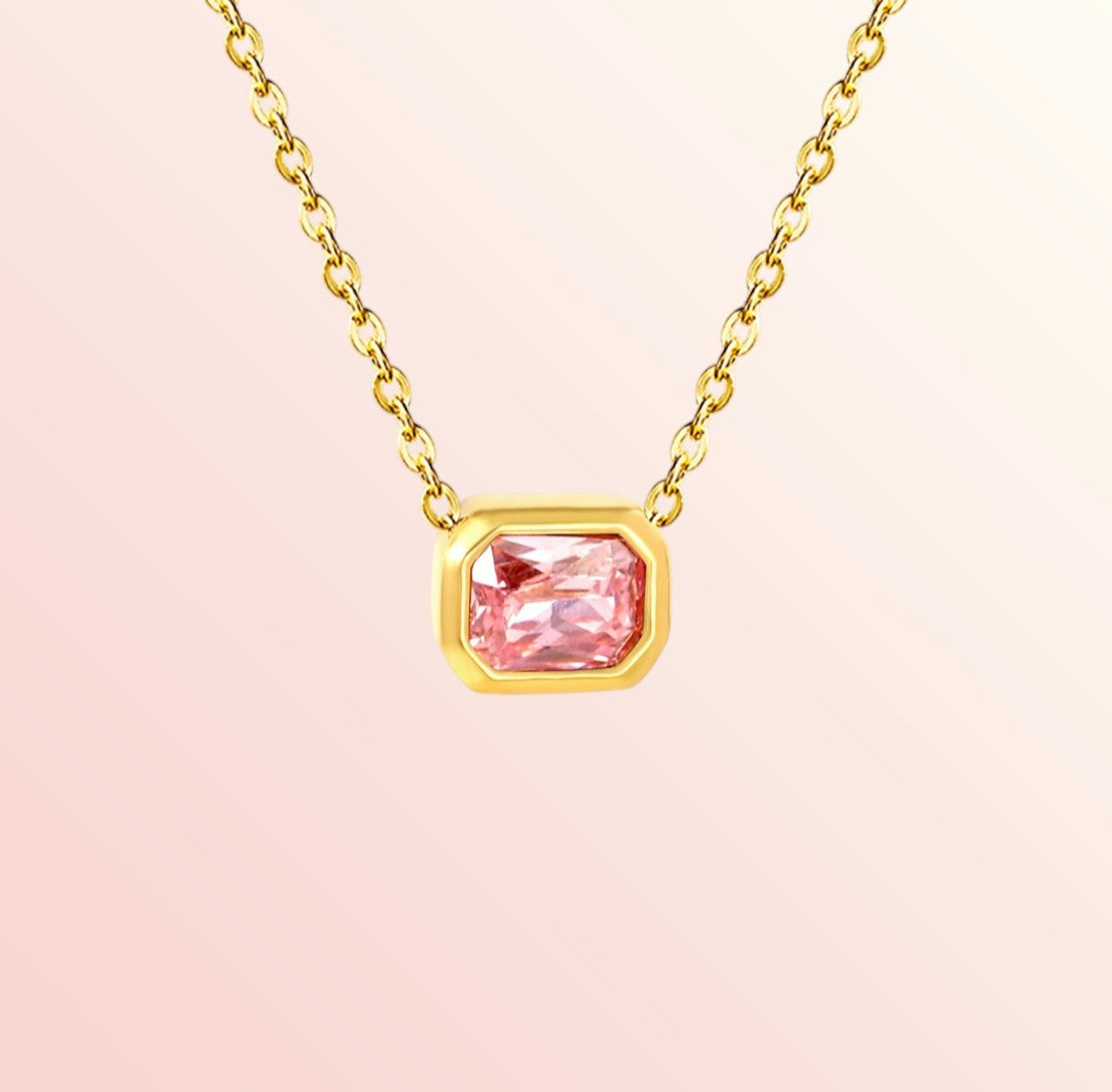 Gold necklace with a pink gemstone on a light pink background