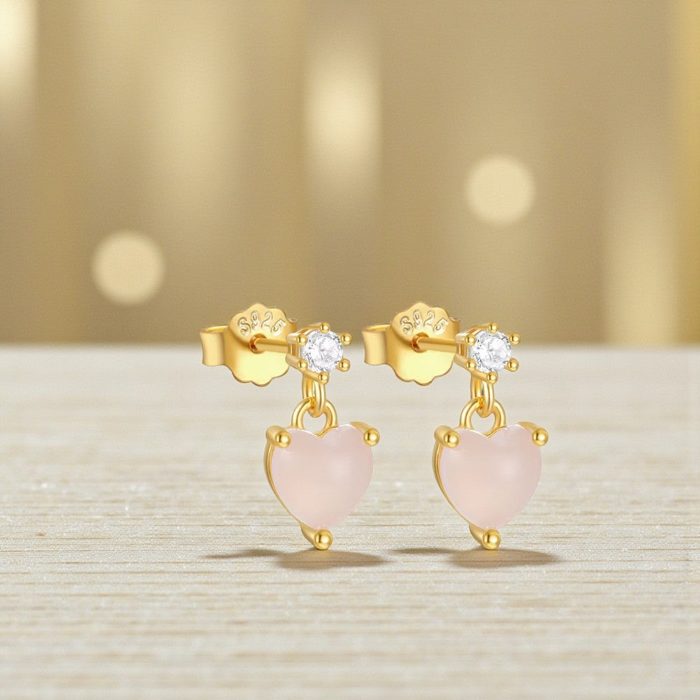 Gold earrings with pink heart-shaped stones on a light background