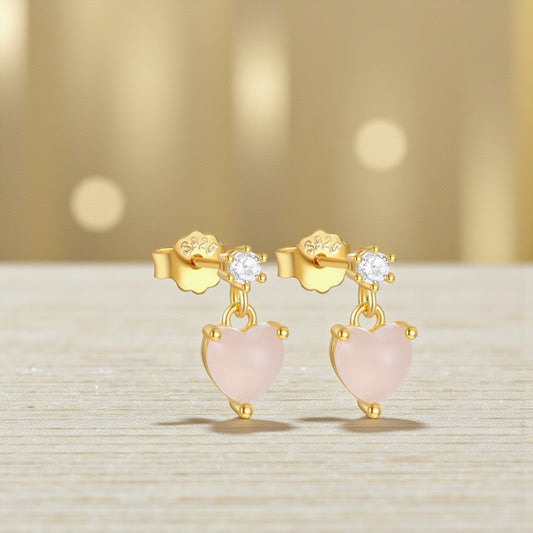 Gold earrings with pink heart-shaped stones on a light background