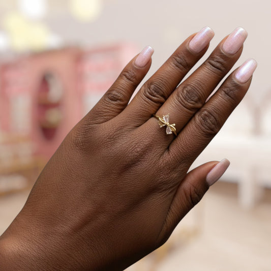 Hand wearing a gold ring with a bow design on a blurred background