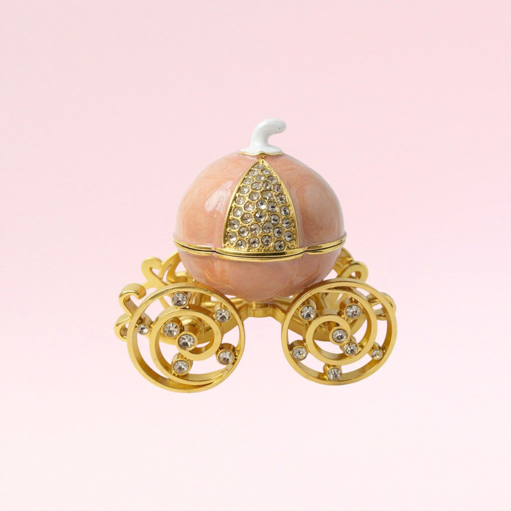 Decorative pumpkin-shaped box with gold accents and gemstones on a pink background
