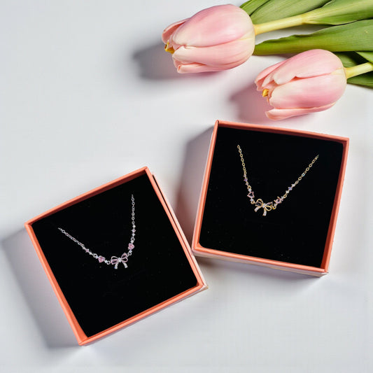 Two bowknot bracelets in open jewelry boxes with pink tulips on a light gray background